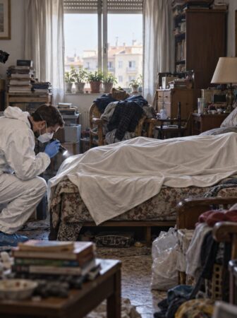 Recreación de dos técnicos forenses examinando un cuerpo cubierto en una vivienda con acumulación extrema.